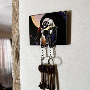 May include: A black and white key holder with a picture of Jack Skellington and Sally from the Nightmare Before Christmas. The key holder has two chains with key rings attached.