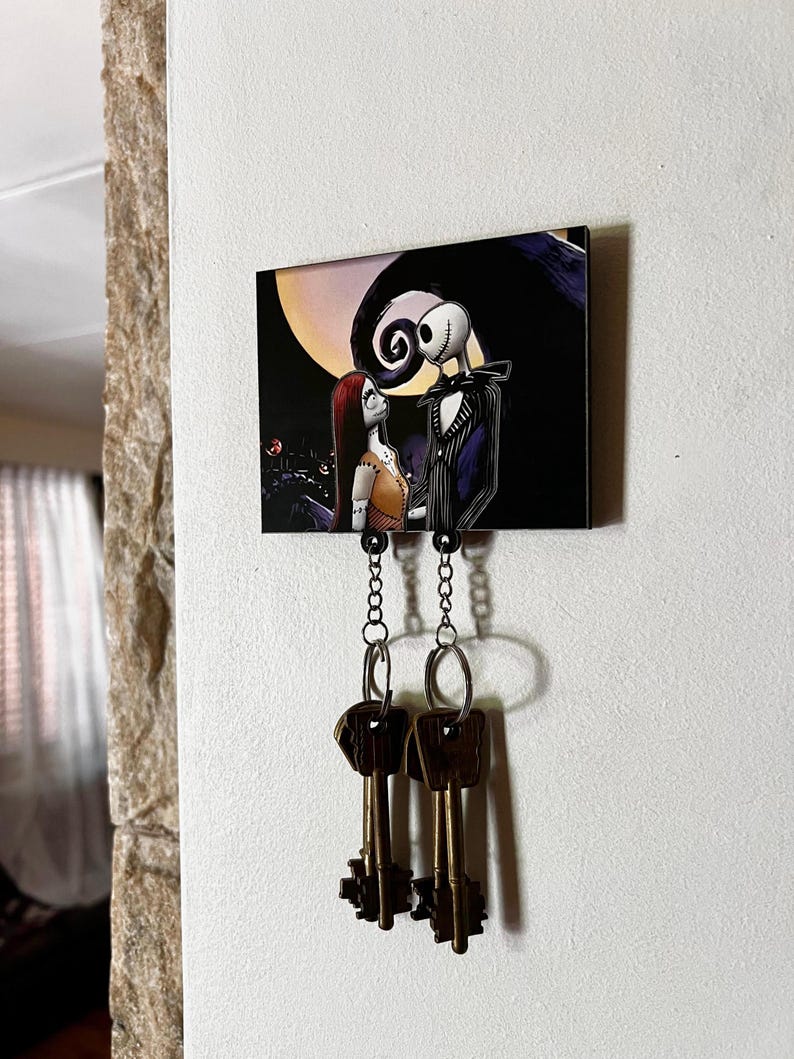 May include: A black and white key holder with a picture of Jack Skellington and Sally from the Nightmare Before Christmas. The key holder has two chains with key rings attached.