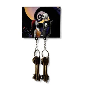May include: A black and white key holder with a picture of Jack Skellington and Sally from The Nightmare Before Christmas. The key holder has two hooks for hanging keys.
