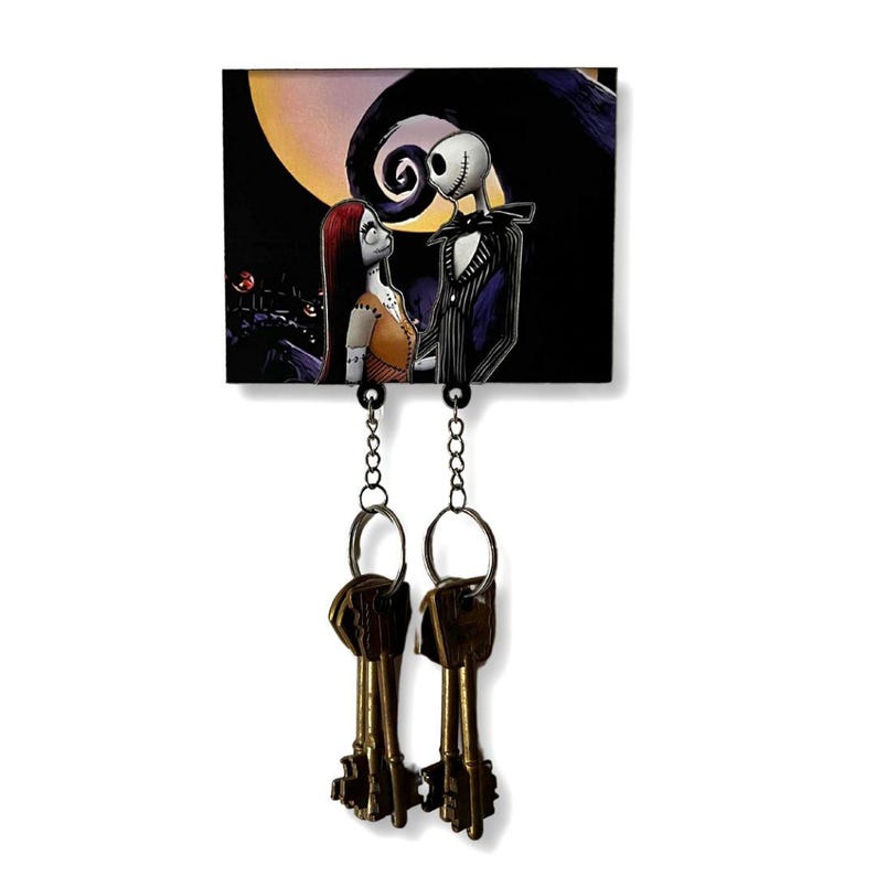 May include: A black and white key holder with a picture of Jack Skellington and Sally from The Nightmare Before Christmas. The key holder has two hooks for hanging keys.