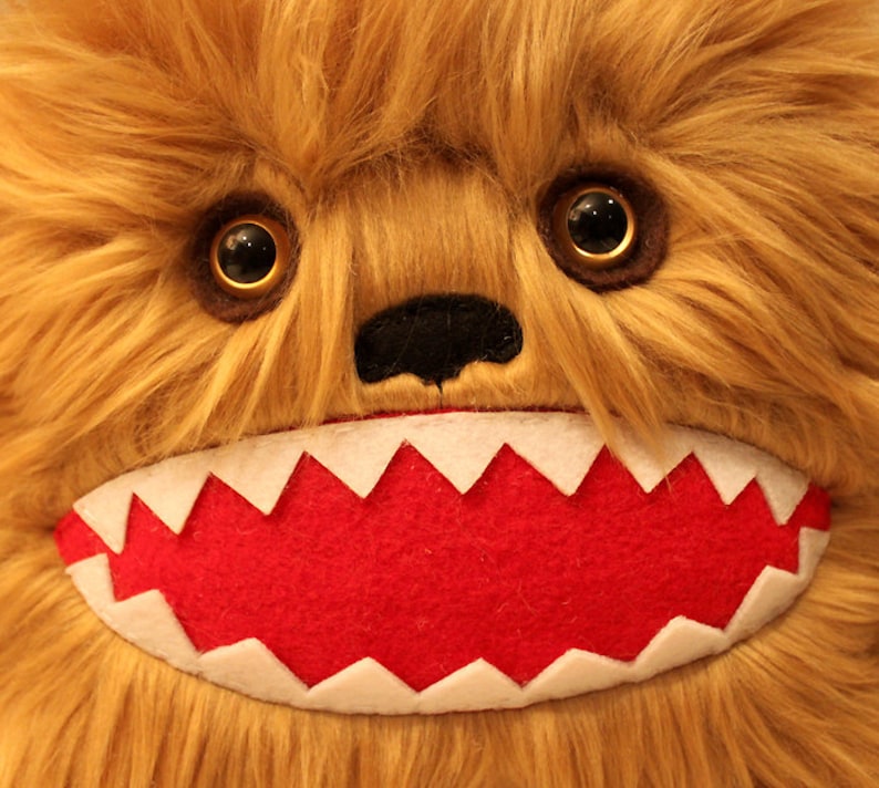 May include: A plush toy with brown fur, large black eyes, and a red mouth with white teeth. The toy has a black nose and a furry face.