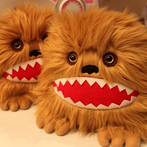 May include: Two brown furry plush toys with large, toothy grins. The toys have red felt mouths with white teeth and black noses.