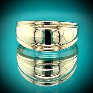 May include: A polished gold ring with a rounded band. The ring reflects the surrounding environment, creating a mirrored effect. The ring is set against a teal background, enhancing its shine.
