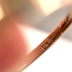 May include: Close-up of a gold ring with the inscription "10K" etched into the band. The ring has a polished finish. The background is blurred.