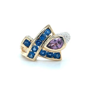 May include: A gold ring with a pear-shaped pink gemstone and a section of small white stones. The ring has a geometric design with blue gemstones set in a gold band. A unique piece of jewellery.