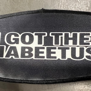 Może przedstawiać: Czarna i szara naszywka z napisem "I GOT THE DIABEETUS" w białych, pogrubionych literach. Naszywka ma czarną obwódkę i teksturowaną powierzchnię.