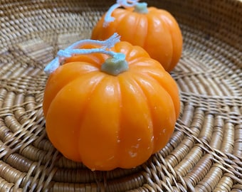 Könnte beinhalten: Zwei orangefarbene, kürbisförmige Seifen mit hellgrünen Stielen und weißen Schnurakzenten. Die Seifen liegen in einem braunen Weidenkorb. Eine festliche Herbst- oder Halloween-Dekoration.