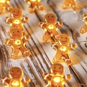 Op de afbeelding: Een reeks warme, gloeiende peperkoekmannetjeslampjes. Elk lampje is doorschijnend oranje met witte accenten en een lachend gezicht. De lampjes zijn geregen op een dunne, transparante draad, perfect voor feestelijke decoratie.