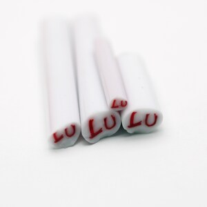 May include: Four white polymer clay sticks with the word "LULU" written in red on each stick.
