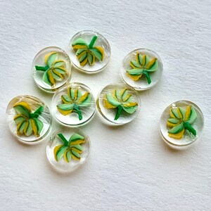 May include: Nine glass buttons with a green and yellow floral design. The buttons are round and have a clear glass base.