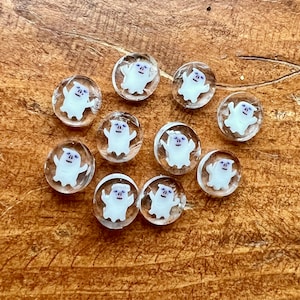 May include: Ten clear glass ghost ornaments with white ghosts and purple eyes. The ghosts are in various poses with their arms raised.