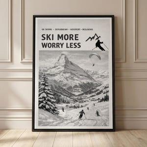 Peut inclure: Affiche encadrée en noir et blanc avec le texte "SKI MORE WORRY LESS". L'image présente un paysage de montagne avec des skieurs, un parapente et une montagne enneigée. Le haut de l'affiche porte les mots "GO SKIING - EXPLORATION - DISCOVERY - WELLBEING".