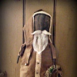 May include: A handmade primitive folk art Santa Claus doll with a brown felt body, white felt beard and a white felt trim around the hood. The doll is holding a small wreath in its hand. Copyright T.H.C. Folk Art 2012.