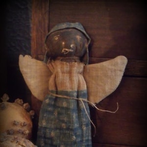 May include: A handmade rag doll angel with a blue and brown dress, brown wings, and a black face. The doll is standing on a green surface.