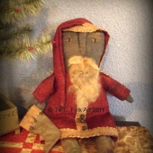 Könnte beinhalten: Eine handgemachte Stoffpuppe Weihnachtsmann, der einen roten Kapuzenmantel mit weißem Besatz und einen langen weißen Bart trägt. Die Puppe hält einen braunen Stiefel in der Hand und sitzt auf einem roten und goldenen Stoff mit Muster.