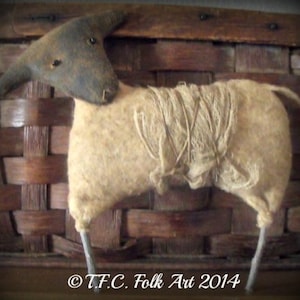 May include: A handmade primitive style lamb figurine with a brown head and a beige wool body. The lamb is standing on a wooden surface. ©T.F.C. Folk Art 2014