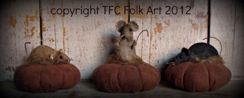 May include: Three handmade fabric pumpkins with mice sitting on top. The pumpkins are brown and the mice are gray, black, and brown. The background is a white wooden wall with the text "copyright TFC Folk Art 2012".