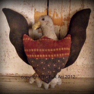 May include: A handcrafted folk art eagle with outstretched wings. The eagle has a gray head and a yellow beak. The chest is a shield shape, with a red and gold striped top and a blue star-studded bottom. The wings are dark brown.