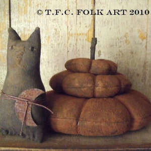 May include: A handmade black cat figurine with a rusty metal crescent moon tied around its waist, standing next to a stack of three brown fabric pumpkins.