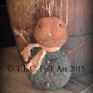 May include: A handmade rag doll snowman with a brown felt head, a blue and white patterned body, and a brown burlap scarf. The snowman is standing on a wooden surface.  © T.F.C. Folk Art 2015