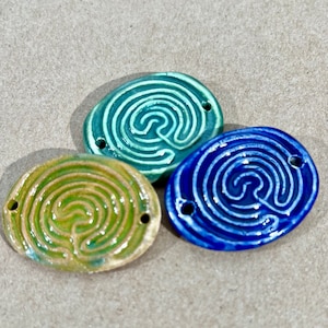 Könnte beinhalten: Drei ovale Anhänger aus Keramik mit einem Labyrinth-Design. Die Anhänger sind in Grün-, Blau- und Gelbtönen gehalten.