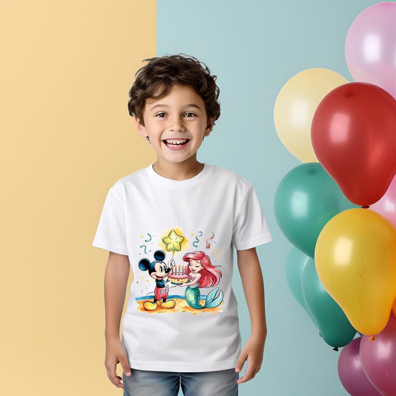 May include: A white t-shirt with a colorful illustration of Mickey Mouse and Ariel the Mermaid holding a birthday cake. There is a yellow star balloon above them.