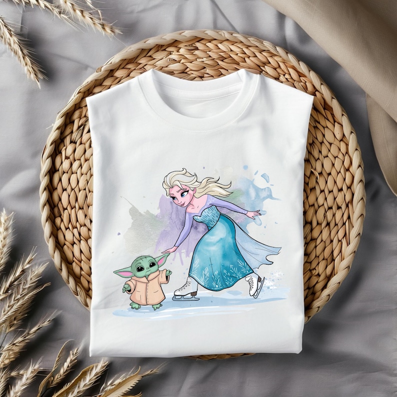 May include: White t-shirt with a watercolor illustration of Elsa from Frozen ice skating with a small green alien character. The alien is wearing a brown coat and is holding out its hand to Elsa.