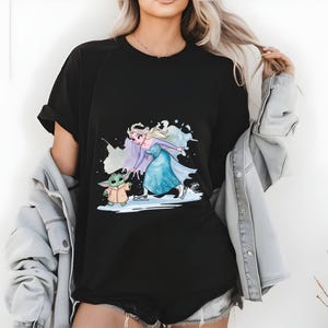 May include: Black t-shirt with a graphic print of Elsa from Frozen ice skating with a small green character from Star Wars. The graphic is in a watercolor style.