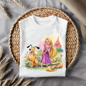Op de afbeelding: Wit T-shirt met een kleurrijke illustratie van een meisje met lang blond haar en een hond. Het meisje draagt een paarse jurk en houdt haar haar vast. De hond is bruin en geel en heeft een lange staart. De achtergrond is in aquarelstijl met een kasteel in de verte.