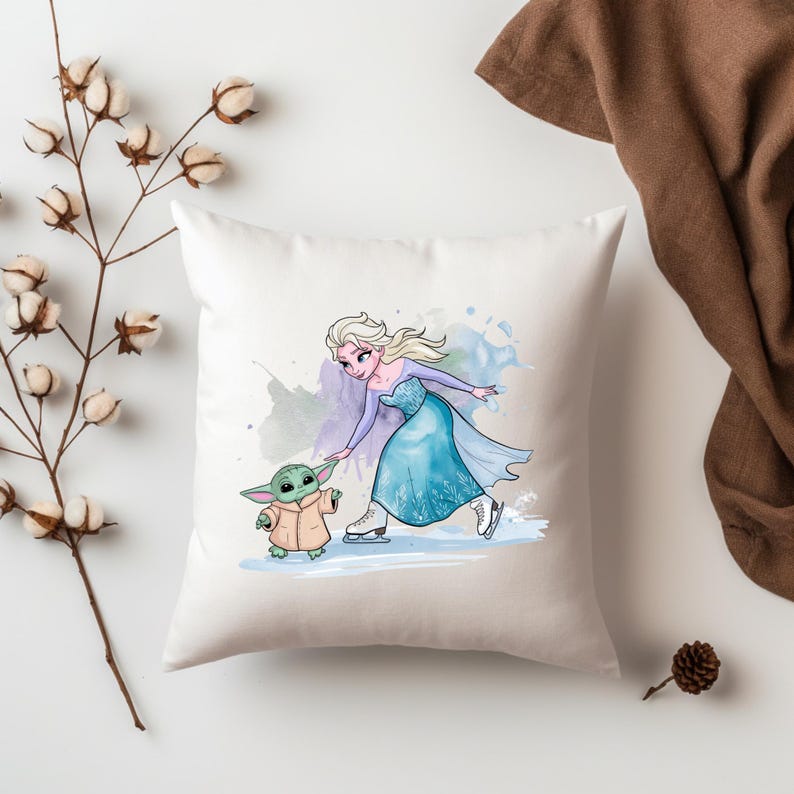 May include: A white throw pillow with a watercolor design of a cartoon Elsa from Frozen ice skating with a small green alien character. The background is a light blue and purple watercolor wash.