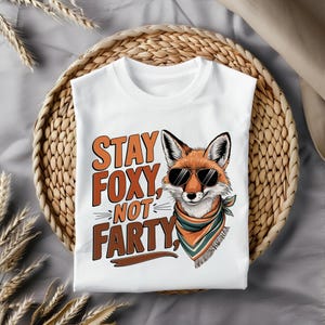 May include: White t-shirt with a graphic of a fox wearing sunglasses and a bandana. The text "Stay Foxy, Not Party" is printed on the shirt.