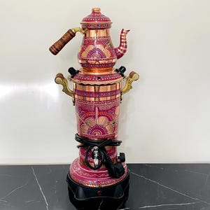 May include: An ornate copper and pink samovar with etched patterns. It has a teapot, wooden handles, and brass details. The base is black. The samovar is a traditional design, likely used for heating water for tea. The height is approximately 50 cm.