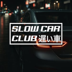 Peut inclure: Vue arrière d'une voiture grise foncée de nuit, avec le texte "SLOW CAR CLUB 遲い車" dans un cadre blanc. Les feux arrière rouges de la voiture sont allumés, et l'arrière-plan est flou avec des lumières de la ville.
