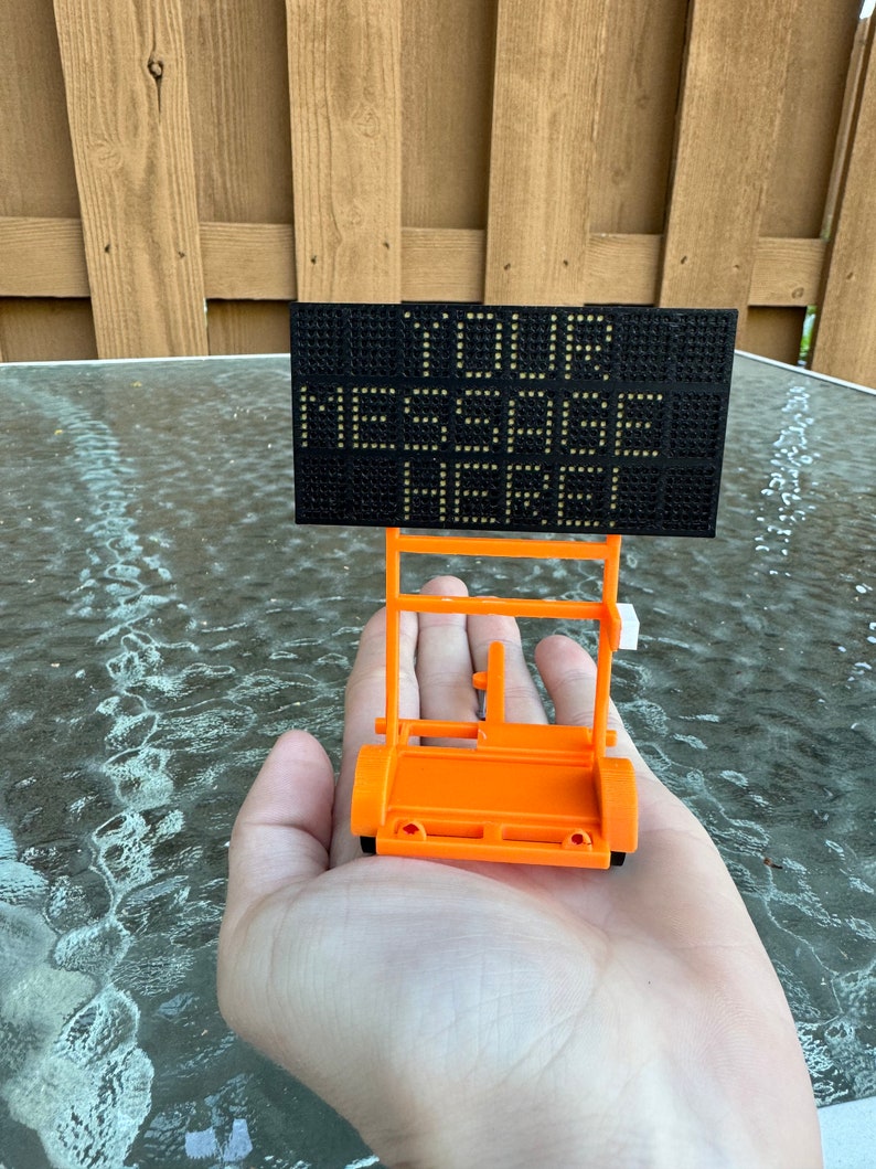 May include: A small orange toy sign with wheels, holding a black sign with white dots that reads "YOUR MESSAGE HERE".