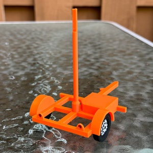 May include: An orange toy trailer with a tall, vertical pole. The trailer has a black wheel on one side and a white wheel on the other side.