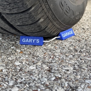 May include: Two blue foam wheel chocks with white string attached. The chocks are labeled "GARY'S" and "GARAGE".