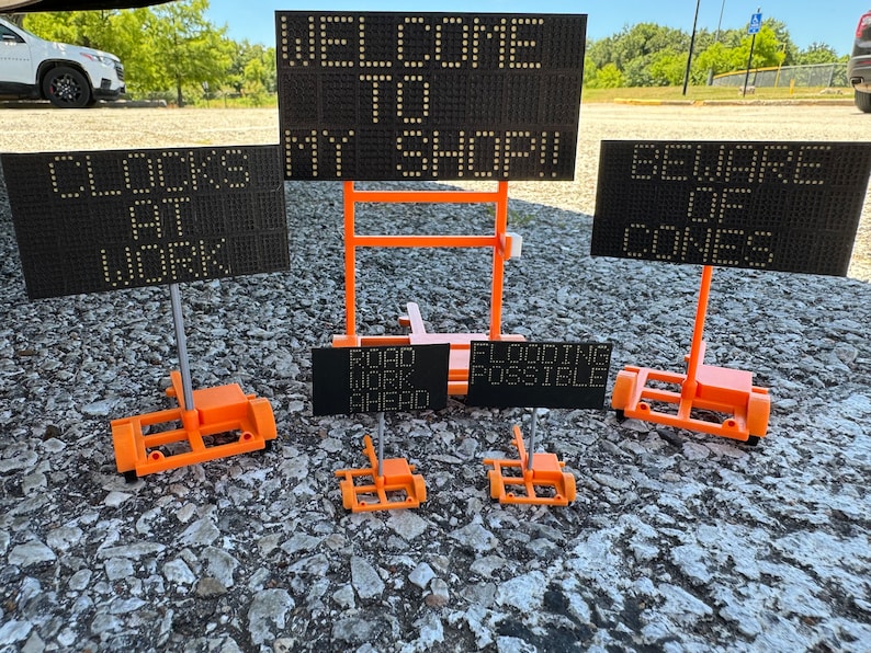 May include: Five orange and black digital message boards with various messages. The messages include "Welcome to My Shop", "Clocks At Work", "Beware of Cones", "Road Work Ahead", and "Flooding Possible".