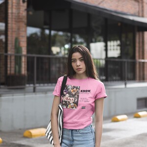 May include: A woman wearing a pink t-shirt with a graphic print of a group of people and the text "KNOW YOURSELF" and blue jeans. The graphic print includes the text "DRAKE".