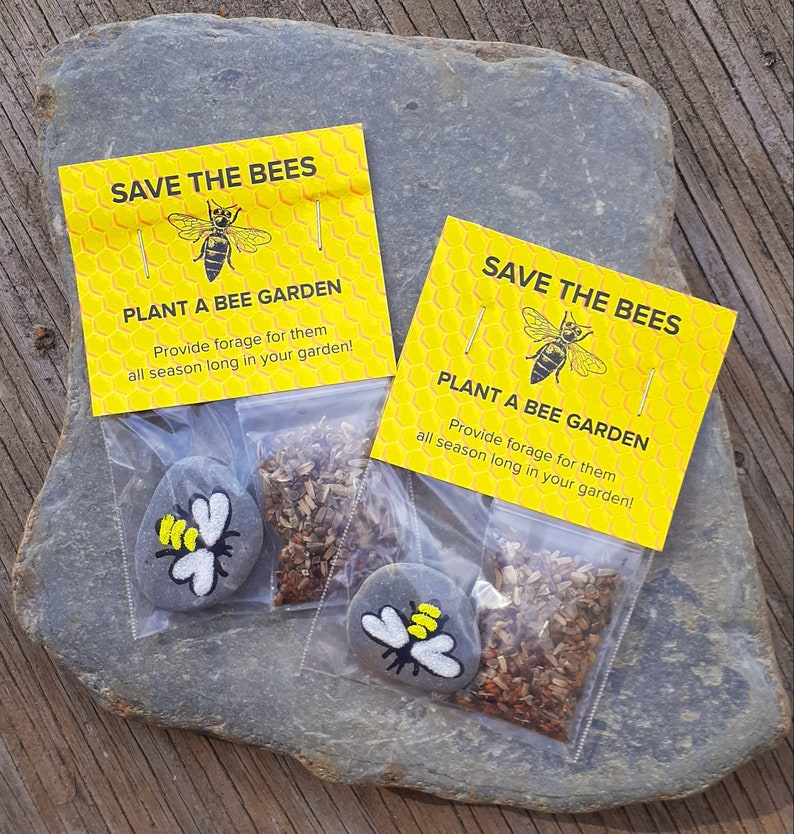 May include: Two small yellow and black bee-themed gift bags with the text "Save the Bees" and "Plant a Bee Garden" on the front. Each bag contains a small gray rock painted with a bee and a packet of wildflower seeds.