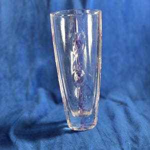 May include: A clear glass vase with a rectangular base and a flared top. The vase has a series of purple glass bubbles running vertically through the center. The vase is set against a blue background.