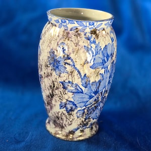 May include: A white ceramic vase with a blue and gold floral pattern. The vase has a rounded body and a flared lip.