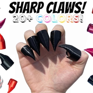 May include: A hand wearing black claw-like finger rings. The image also shows several other claw rings in various colors, including red, pink, and black. The text "SHARP CLAWS! 20+ COLORS!" is visible in the image.