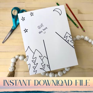 May include: A white paper with a black line drawing of trees, stars, and a crescent moon. The text "GLUE ship here" is handwritten on the paper. A pair of blue scissors, pencils, and a beaded garland are on a wooden surface.