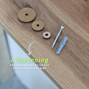 May include: A close-up of a wooden wall mount system with three wooden circles, a screw, and a plastic anchor. The text "A fastening that allows you to rotate the frame on the wall" is written below the items.