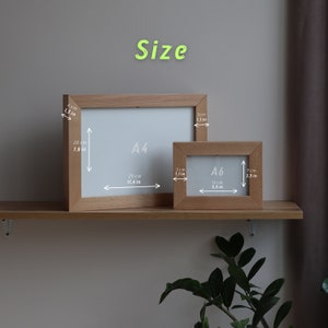 May include: Two wooden picture frames, one labeled "A4" and the other "A6", with measurements in inches and centimeters. The frames are on a wooden shelf.
