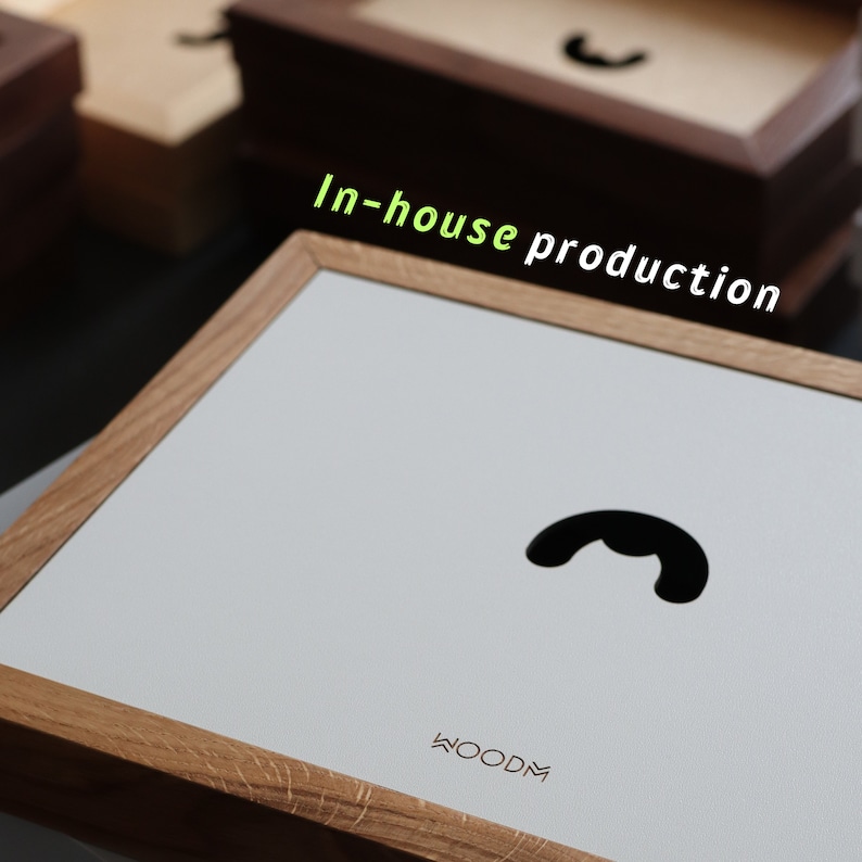 May include: A light wood frame with a white background and a black silhouette of a phone receiver. The text "WOODM" is printed in the bottom right corner of the frame. The text "In-house production" is written in green letters above the frame.