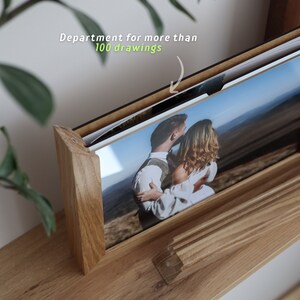 May include: A wooden photo album with a black frame and a photo of a couple embracing in a field. The album is designed to hold more than 100 photos.