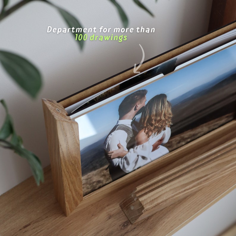 May include: A wooden photo album with a black frame and a photo of a couple embracing in a field. The album is designed to hold more than 100 photos.