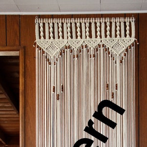 May include: White macrame wall hanging with brown wooden beads. The macrame is made with a simple knot pattern and hangs from a wooden dowel.