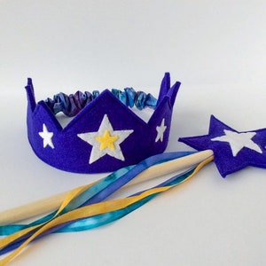May include: A purple felt crown with white stars and a yellow center star. A matching purple felt star wand with a white star and a wooden stick with blue, yellow, and teal ribbons.